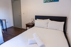 Ett hotellrum med en säng, ett nattduksbord, en lampa och en tavla på väggen.