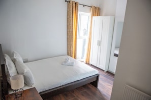 Ein Schlafzimmer mit Bett, Kissen, Lampe, Kleiderschrank und Vorhängen.
