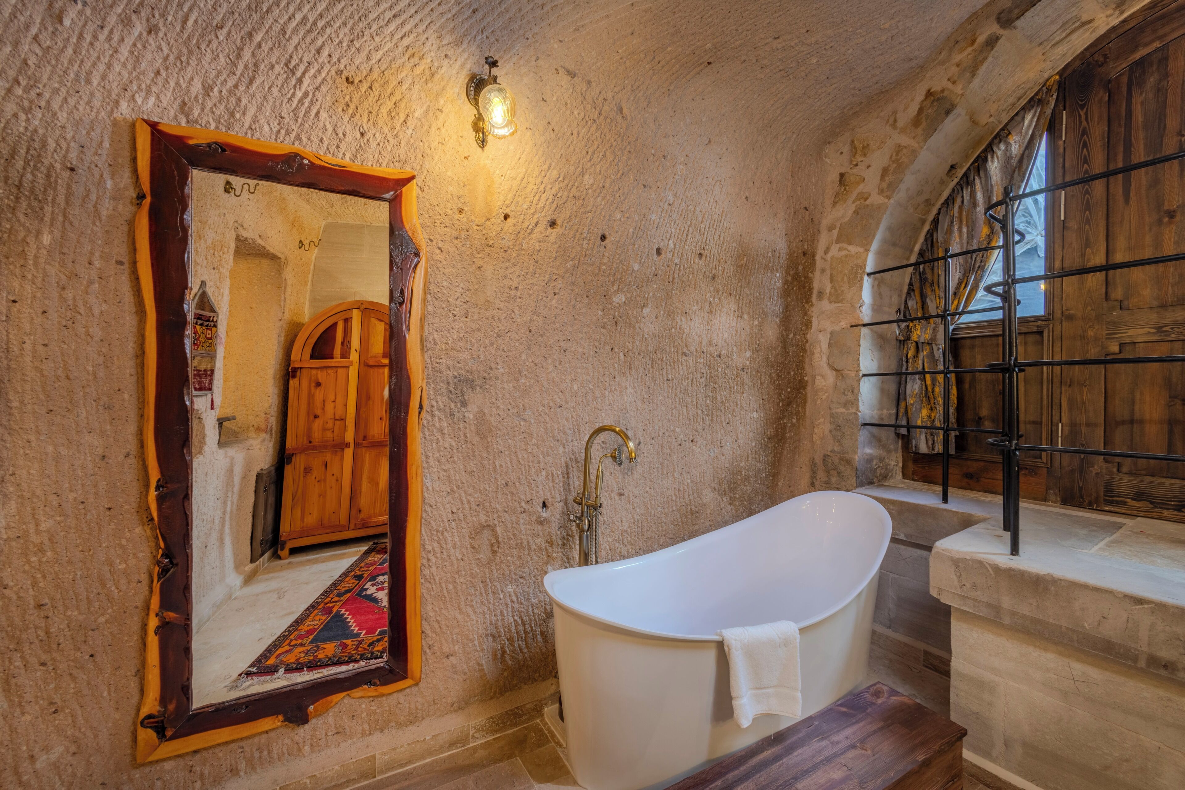 Un baño con una bañera independiente, un armario de madera y un espejo con marco decorativo.