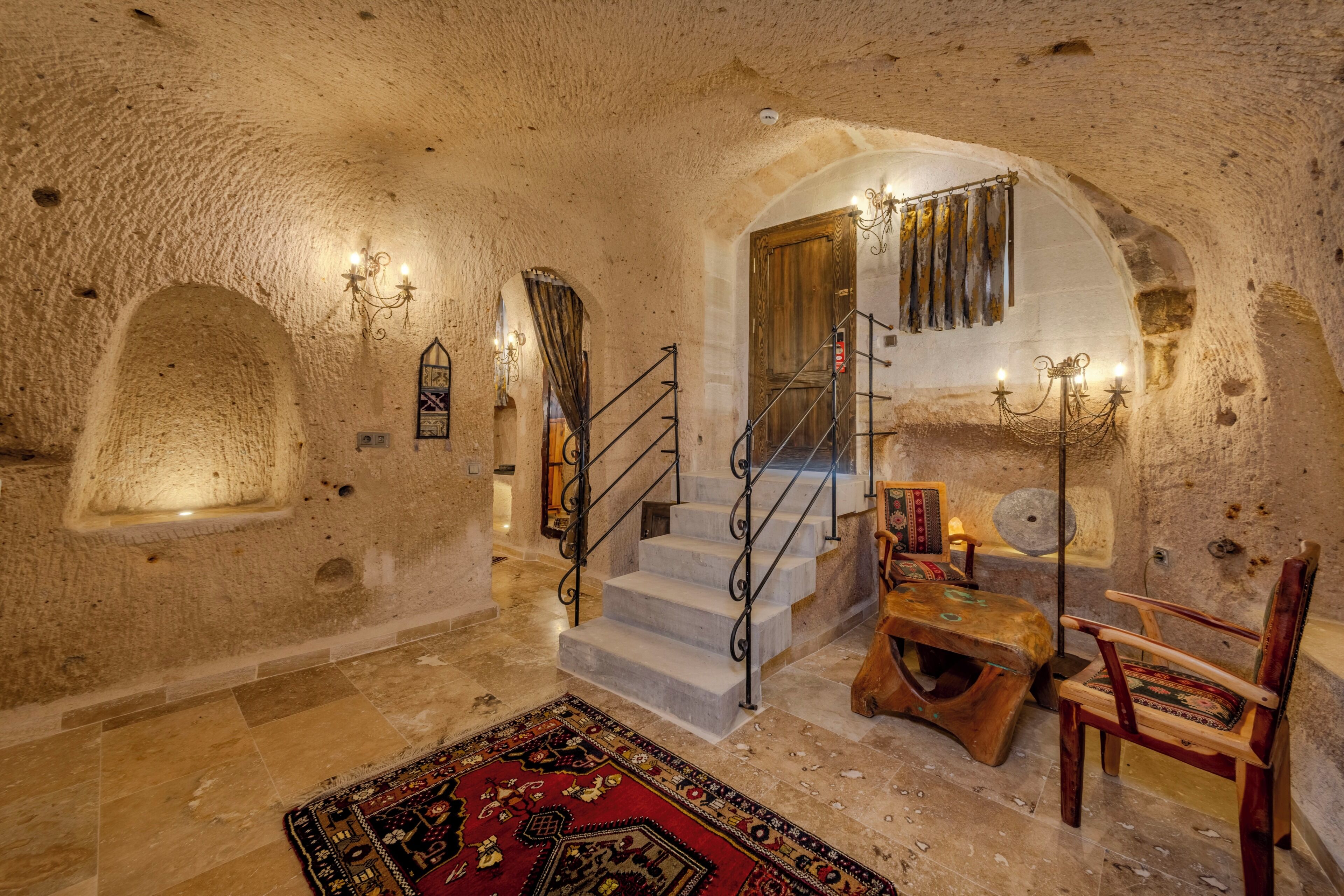 A stone-walled interior with a staircase, a wooden bench, and a patterned rug.