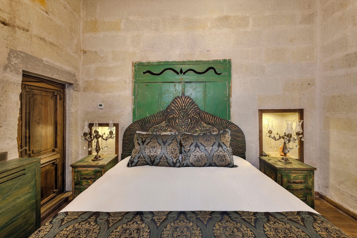 A room with a large bed, two nightstands with lamps, a wooden wardrobe, and a green headboard.