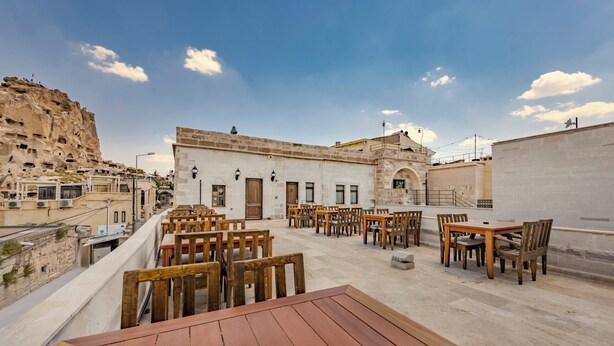 A rooftop terrace with wooden tables and chairs, a stone building in the background, and a clear sky. - VETUS CAVE CAPPADOCIA (NEVŞEHIR)