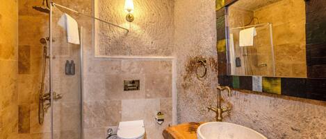 A bathroom with a glass-enclosed shower, a wooden vanity with a stone sink, and a mirror with a mosaic frame.