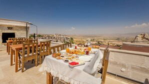 Mesa de jantar montada ao ar livre, com vista para um horizonte urbano e montanhas ao fundo.