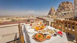 A table set for a meal with a view of a rocky landscape and a building with cave dwellings. - VETUS CAVE CAPPADOCIA (NEVŞEHIR)
