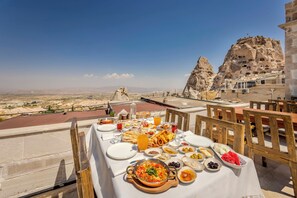A table set for a meal with a view of a rocky landscape and a building with cave dwellings. - VETUS CAVE CAPPADOCIA (NEVŞEHIR)