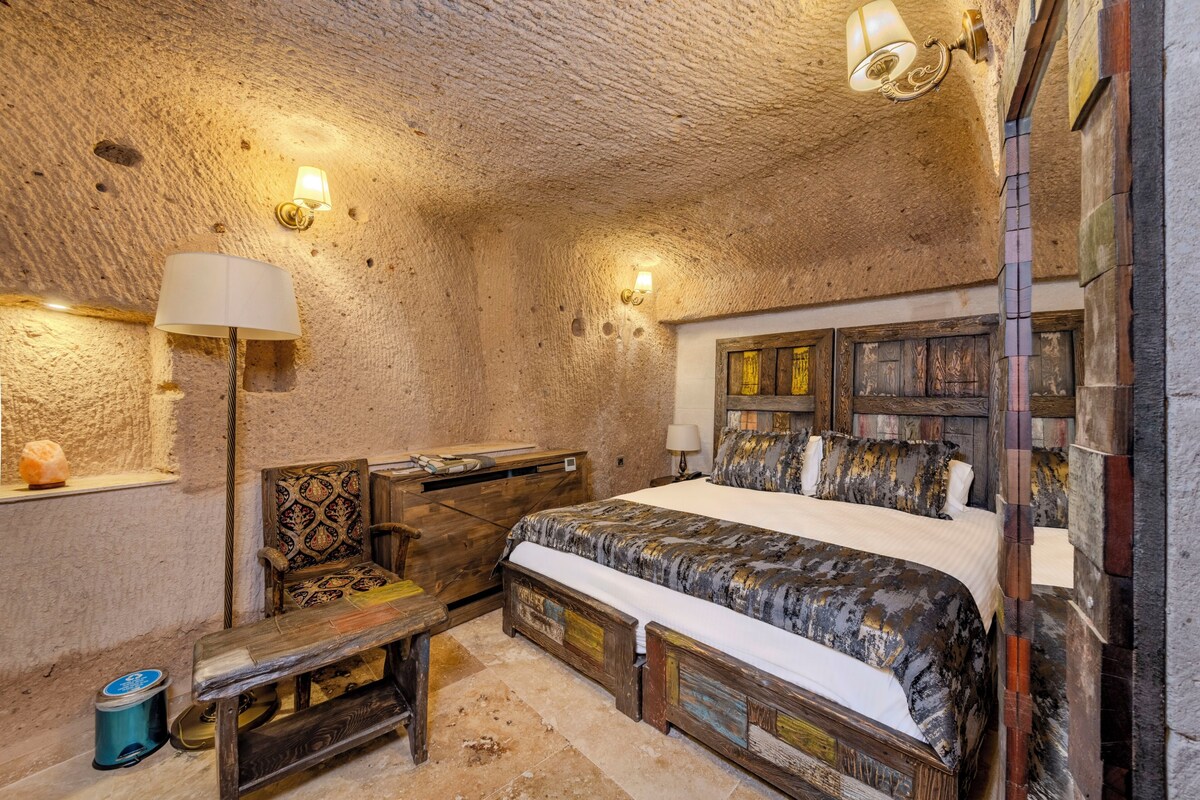 A rustic room with a bed, a chair, a desk, and a lamp.