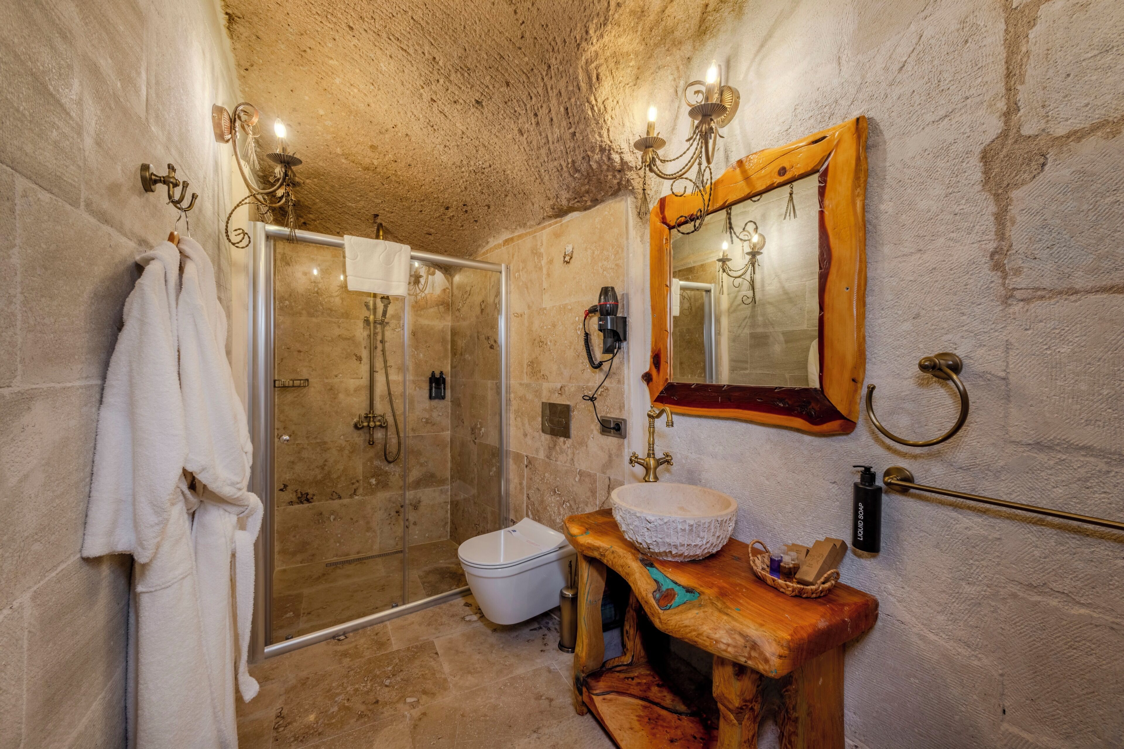 Un baño con ducha envuelta en vidrio, un tocador de madera con lavabo y un espejo montado en la pared.