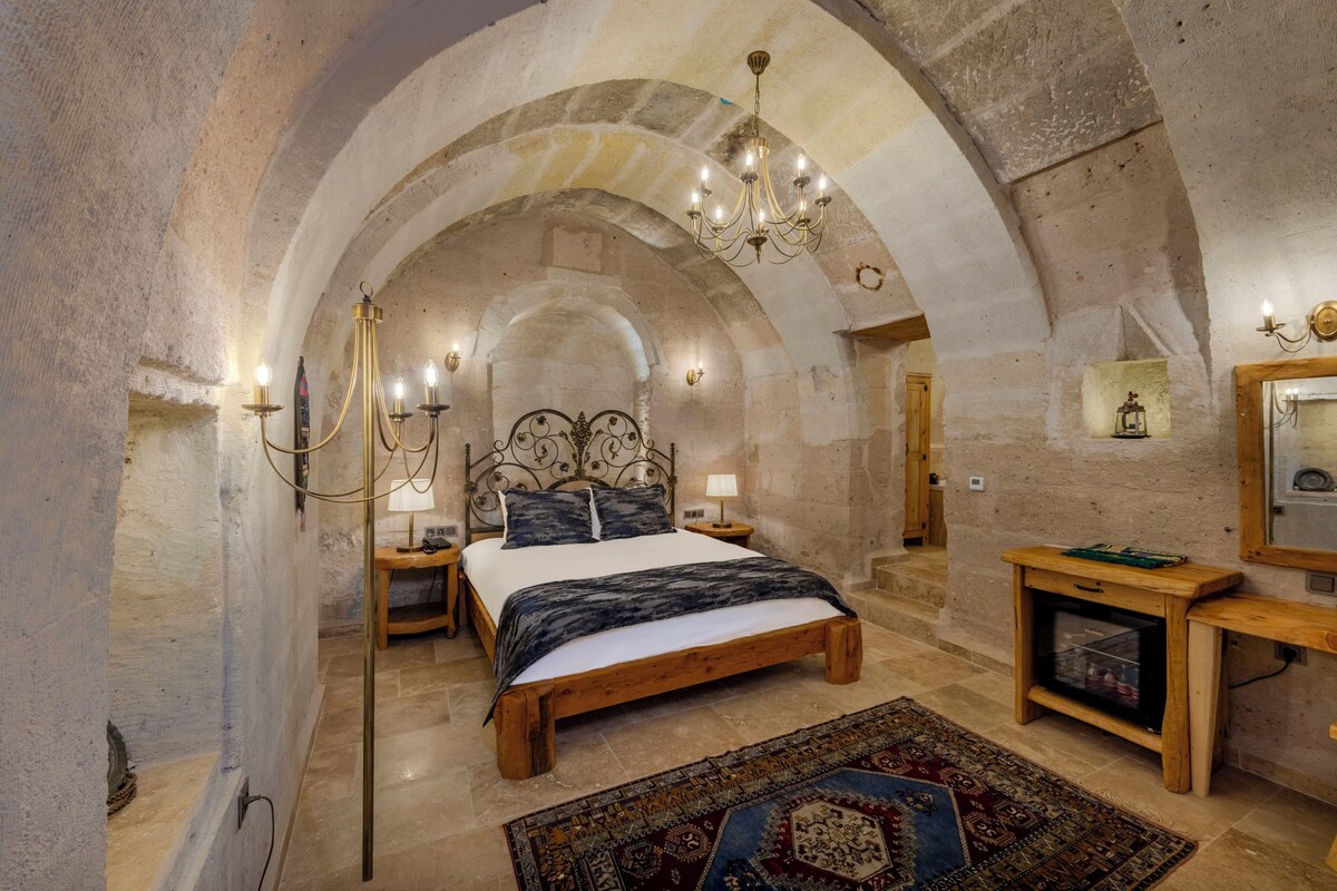 A bedroom with a stone arch ceiling, a wooden bed, a nightstand, a lamp, a mirror, and a television.