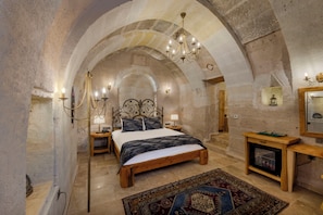 Un dormitorio con techo de arco de piedra, una cama de madera, una mesita de noche, una lámpara, un espejo y un televisor.