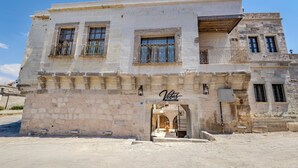 A two-story building with a stone facade, a sign reading 'Vetus Cave Cappadocia,' and a small entrance with steps leading up to it. - VETUS CAVE CAPPADOCIA (NEVŞEHIR)