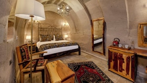 A bedroom with a large bed, a wooden dresser, a mirror, and a chandelier. - VETUS CAVE CAPPADOCIA (NEVŞEHIR)
