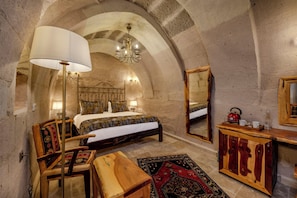 A bedroom with a large bed, a wooden dresser, a mirror, and a chandelier. - VETUS CAVE CAPPADOCIA (NEVŞEHIR)