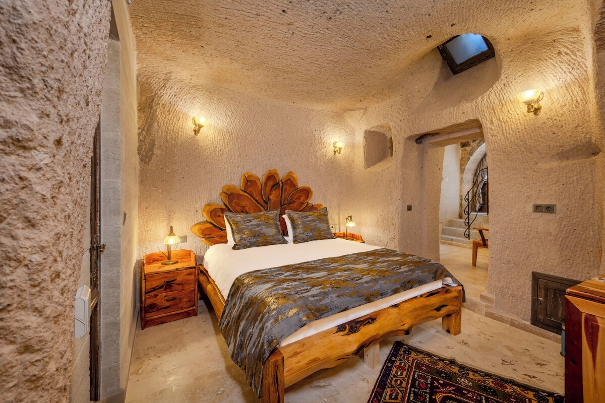 A bedroom with a wooden bed, a nightstand, a TV mounted on the wall, and a patterned rug.