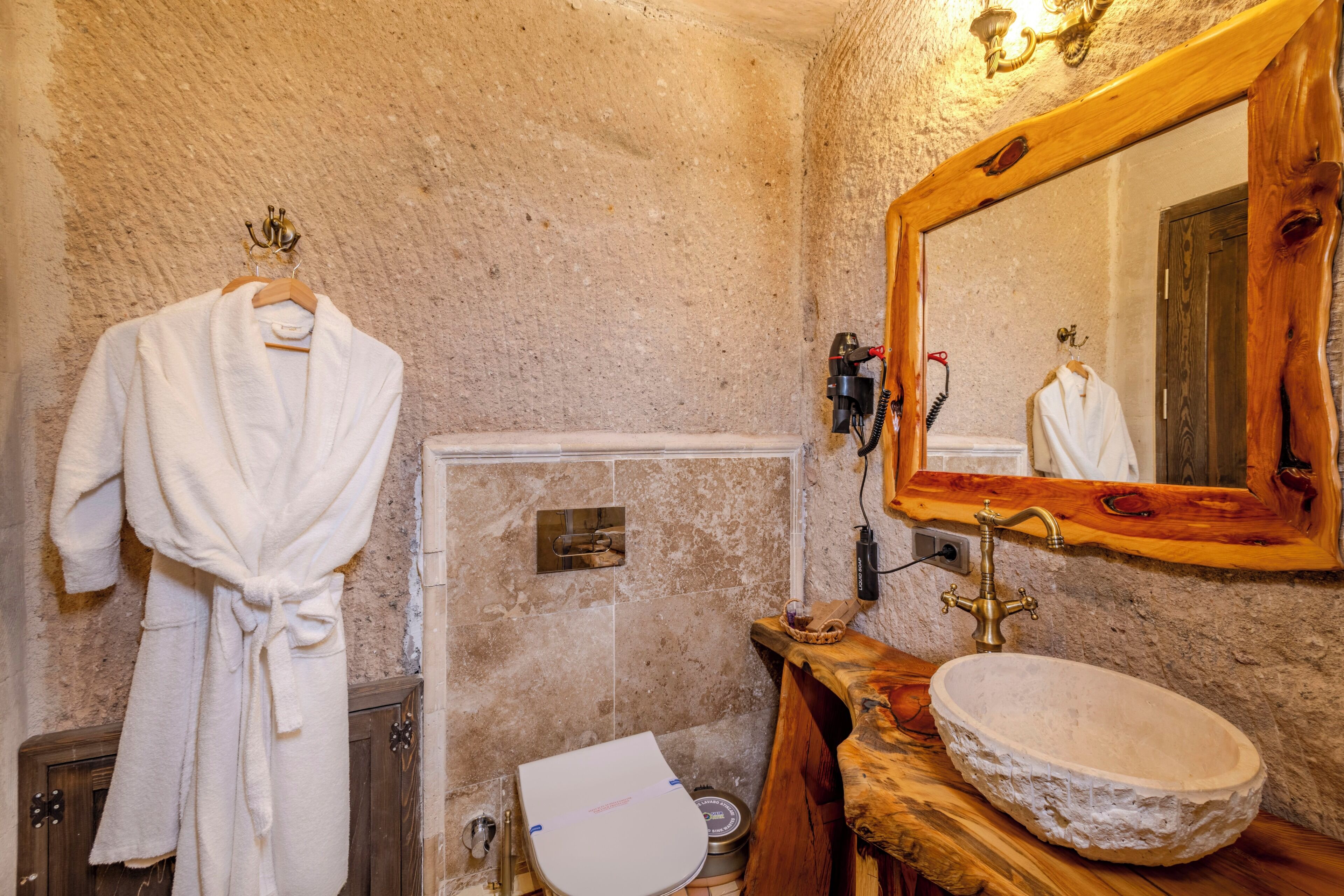 A bathroom with a stone wall, a wooden vanity, a white sink, a towel rack, and a mirror.