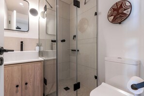 Een moderne badkamer met een glazen douchecabine, een houten wastafelmeubel en een toilet.