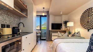 A modern hotel room with a kitchenette, a bed with patterned bedding, a TV, and a view of the outdoors. - Neo-African studio in Cape Town with spectacular rooftop swimming views (Cape Town)
