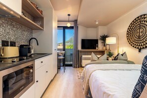 Een moderne hotelkamer met kitchenette, een bed met decoratieve beddengoed, een televisie en uitzicht op de omgeving.