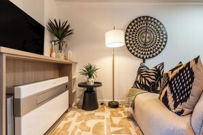Een moderne woonkamer met een flatscreen televisie, een bank met gestreepte kussens, een vloerlamp en een decoratief wandobject.