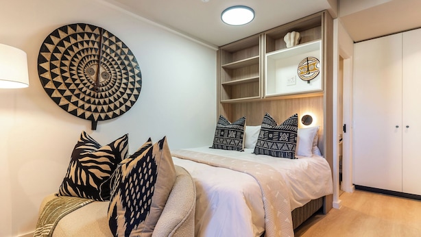 A bedroom with a bed, pillows, a wall art piece, and built-in shelving. - Neo-African studio in Cape Town with spectacular rooftop swimming views (Cape Town)