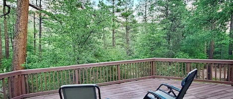 A deck with two chairs and a small table, surrounded by a wooden railing, overlooking a forested area.