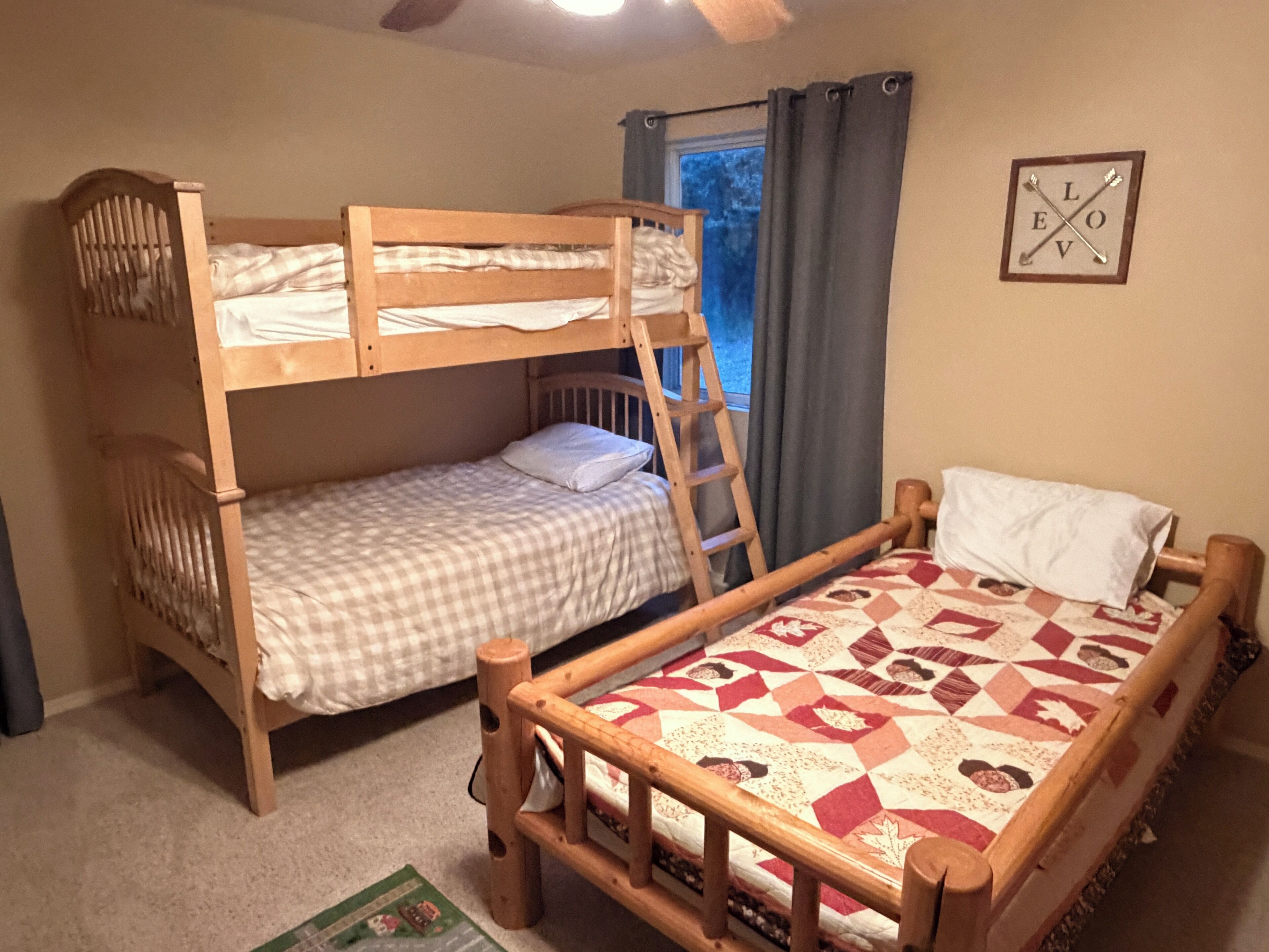 A room with two bunk beds, a ladder, a window with curtains, and a framed picture on the wall.