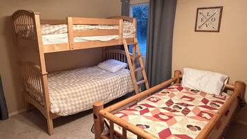 A room with two bunk beds, a ladder, a window with curtains, and a framed picture on the wall.