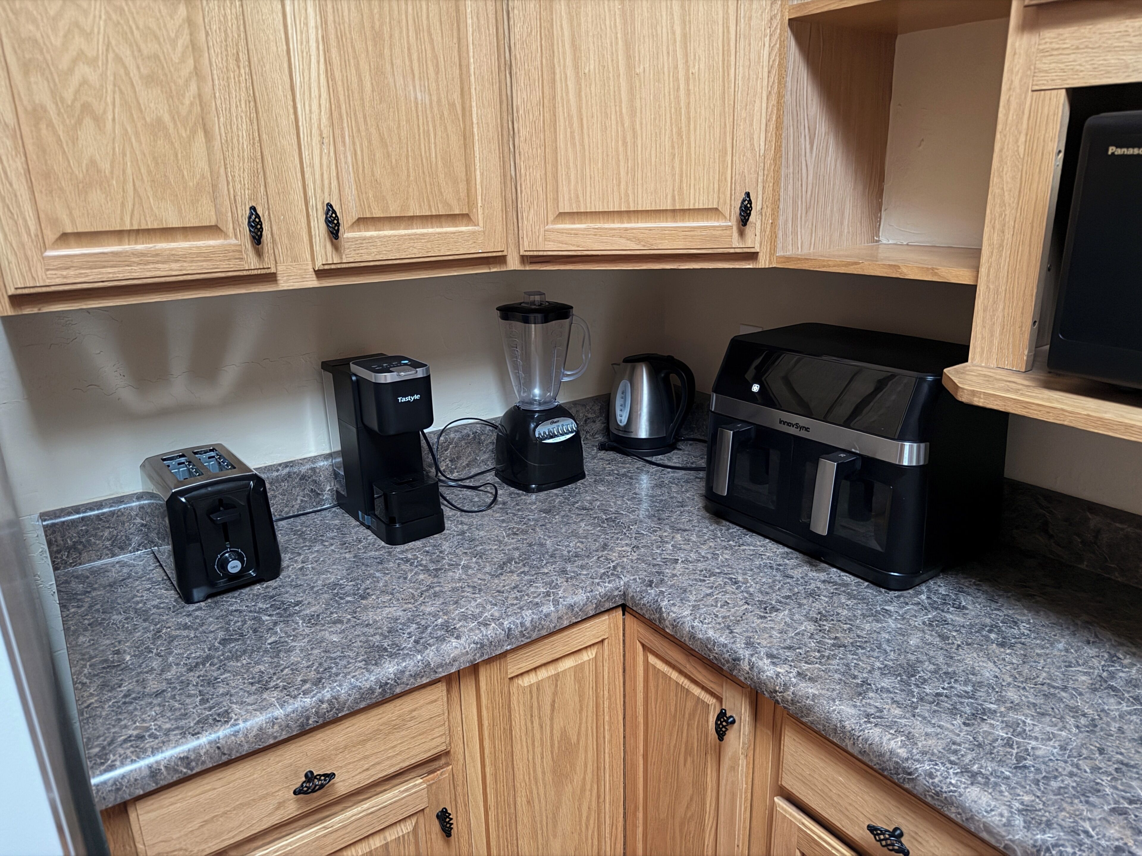 Una cocina con armarios de madera, un tostador, una licuadora, un hervidor y un microondas.
