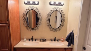 Un baño con dos lavamanos, tocador y espejo con detalles decorativos.