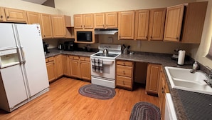 Cocina compacta con muebles de madera, un refrigerador blanco, un microondas, una estufa y un lavabo.