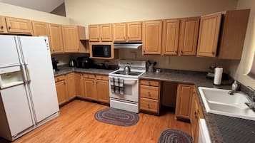 A compact kitchen with wooden cabinets, a white refrigerator, a microwave, a stove, and a sink.