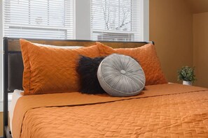 Ein Bett mit einer orangefarbenen gesteppten Bettdecke, zwei orangenen Kissen und einem grauen, geprägten Kissen.