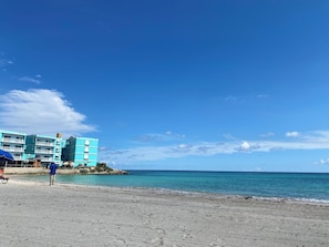 Ein Strandhotel mit Pool, eine Person steht am Pool, und ein klarer, blauer Himmel.