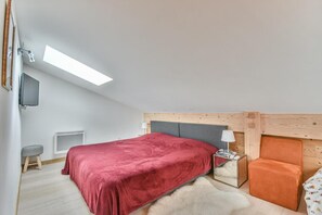 A bedroom with a bed, a nightstand, a lamp, a chair, a small stool, a TV, and a skylight. - 100m from ski slopes, 2nd floor, terrace, tv, 78m², Les Gets (Les Gets)
