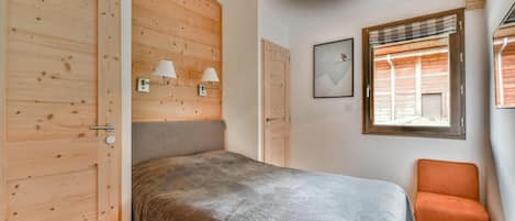 Un dormitorio con cama, paredes de madera, ventana con persianas, una silla y lámparas de pared.