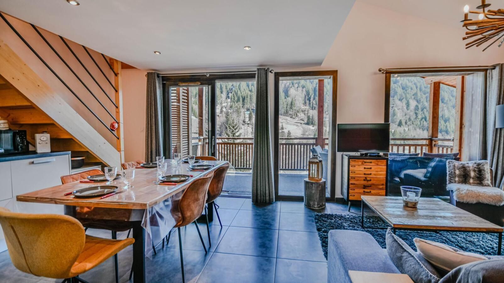 A modern interior with a dining area, a living room, and a balcony with a view of a forested area.