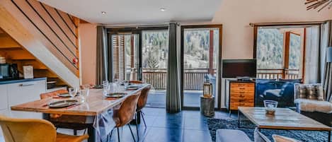 Un intérieur moderne comprenant un coin repas, un salon et un balcon offrant une vue sur une zone boisée.