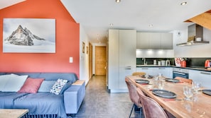 A modern interior with a sofa, dining table, kitchen, and a mountain painting on the wall. - 100m from ski slopes, 2nd floor, terrace, tv, 78m², Les Gets (Les Gets)