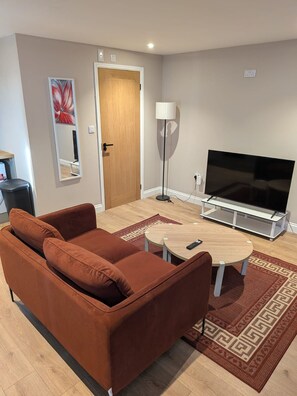 A living room with a sofa, a TV, a lamp, and a door. - Kestrel Cottage - Rural Getaway with Big Garden (Wimblington)