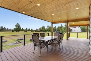 Une terrasse extérieure couverte, avec une table et des chaises, donnant sur une pelouse arborée et une maison en arrière-plan.