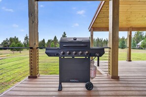 Una parrilla NEXGRILL sobre una terraza de madera, con vistas a un campo cubierto de césped y árboles.