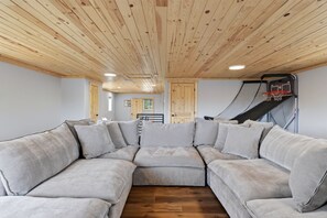 Una habitación con sofá modular, techo de madera y aro de baloncesto.