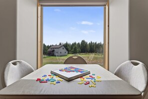 A room with a table set for a game, a window with a view of a house and trees, and two chairs. - Yellowstone Retreat w/AC & wrap-around porch. Fly fish, trail riding, snowmobile (Island Park)