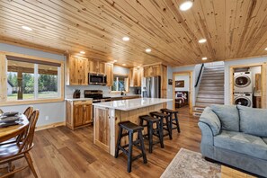 A modern kitchen with wooden cabinets, a central island, and bar stools. - Yellowstone Retreat w/AC & wrap-around porch. Fly fish, trail riding, snowmobile (Island Park)