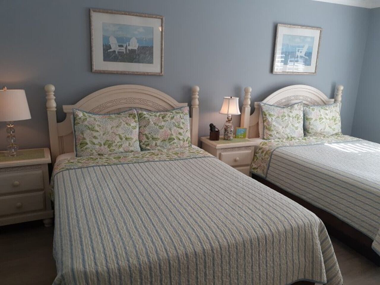 A bedroom with two beds, each with a headboard and a bedside table with a lamp.