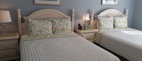 A bedroom with two beds, each with a headboard and a bedside table with a lamp.