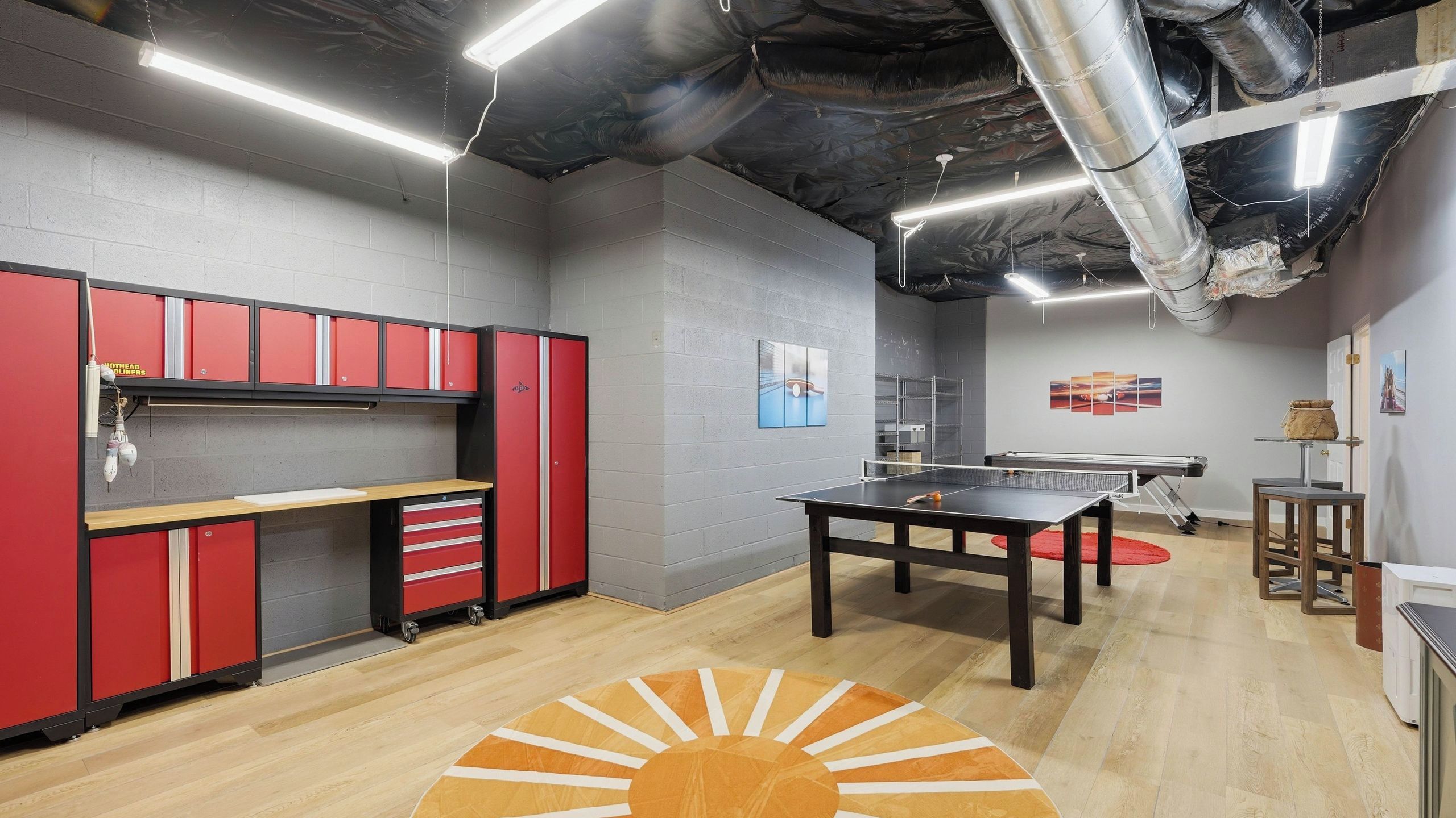 A room with a ping pong table, red storage cabinets, and artwork on the walls.