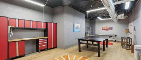 A room with a ping pong table, red storage cabinets, and artwork on the walls.