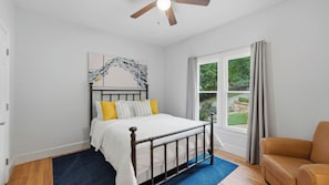 A bedroom with a bed, a ceiling fan, a window with curtains, and a view of greenery outside. - Point of View by Avantstay Private Dock + Kayaks + Hot Tub Lakefront Game Room + Cabana + BBQ (Mooresville)