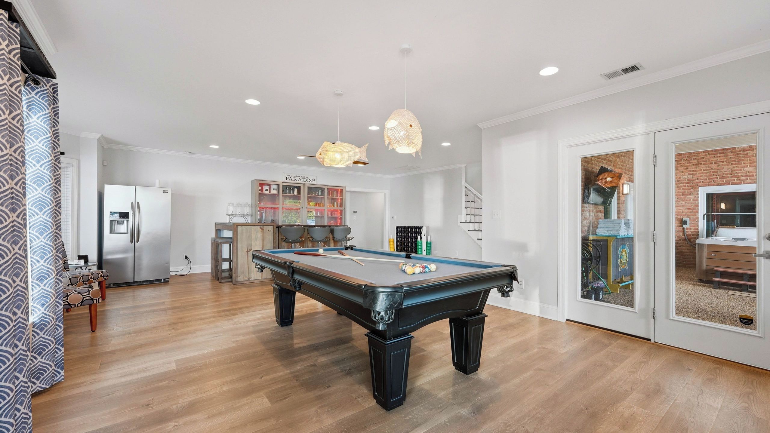 A spacious living area with a pool table, a kitchen with a refrigerator, and a bar area.